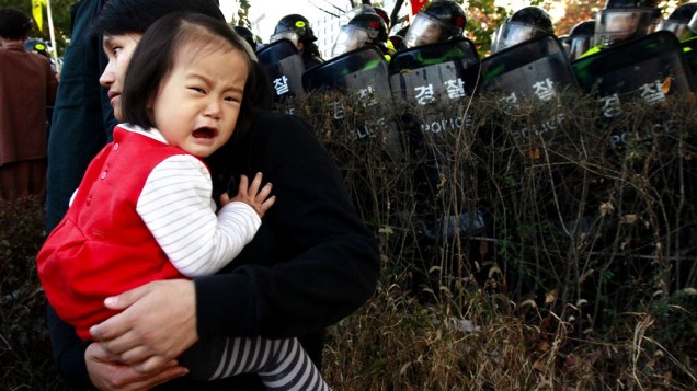 Criança chora no colo da mãe durante enfrentamento da polícia com participantes de marcha contra o Tratado de Livre Comércio em Seul, Coreia do Sul
