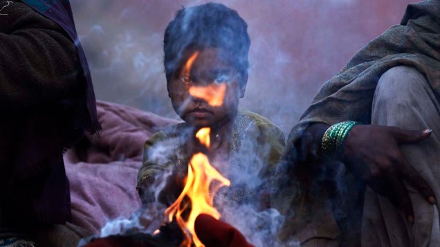 Garoto se aquece em fogueira durante manhã de inverno nos bairros antigos de Nova Délhi, Índia