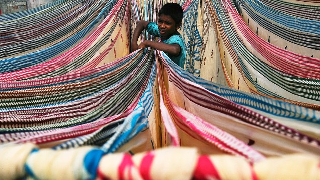 Um menino separa tecidos deixados para secar no telhado de uma fábrica de algodão em Hyderabad, na Índia