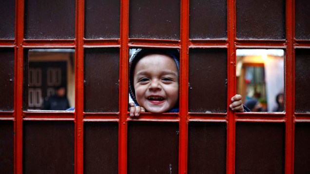 Criança no portão de entrada de monastério tibetano em Katmandu, Nepal