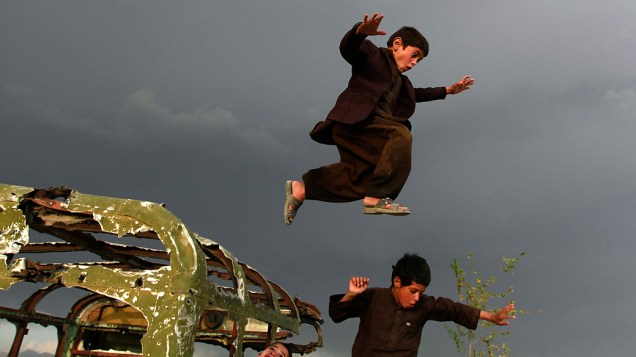 Crianças afegãs pulam por carro destruído em Cabul, no Afeganistão