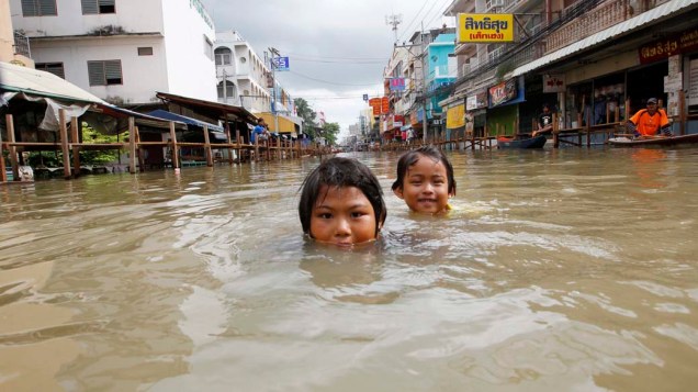 Crianças brincam em rua inundada na cidade de Sena, Tailândia. O país está sofrendo com fortes chuvas e inundações, que já mataram 82 pessoas