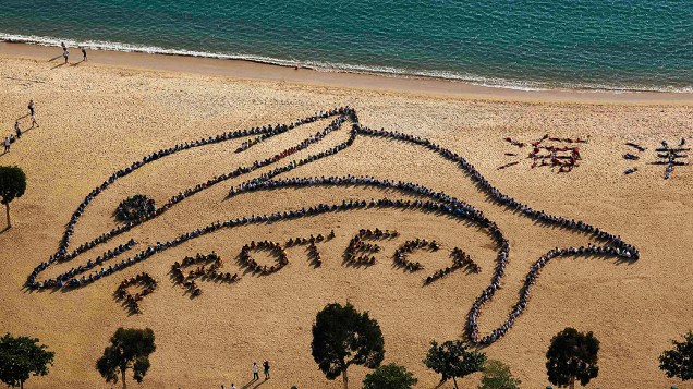 Crianças e estudantes formam o desenho de um golfinho e a palavra Proteja, em praia de Hong Kong. A ação foi feita para elogiar o governo quanto à decisão de banir a pesca de golfinhos com rede na região
