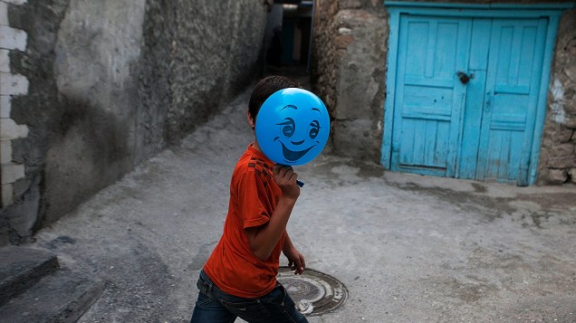 Menino esconde o rosto atrás de um balão em uma rua na vila de Gimry, na Rússia