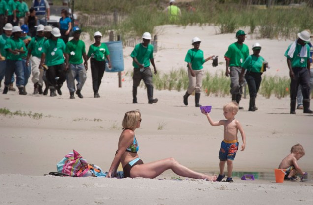 Mulher e crianças brincam em praia no Alabama enquanto trabalhadores realizam limpeza da costa atingida pelo vazamento de óleo da plataforma Deepwater Horizon, nos Estados Unidos. (Foto: Lee Celano/Reuters) - Qual é a gravidade do derramamento de óleo?