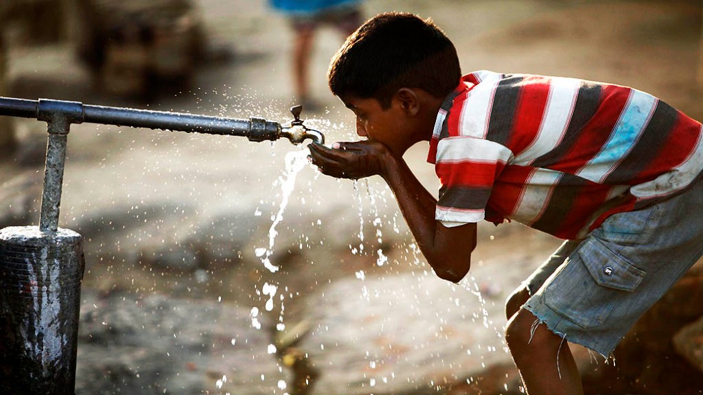 Garoto indiano bebe água de uma torneira em uma estrada em Allahabad, na Índia, no Dia Mundial da Água