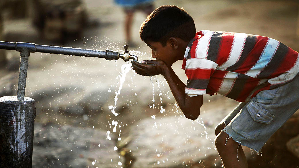 Garoto indiano bebe água de uma torneira em uma estrada em Allahabad, na Índia, no Dia Mundial da Água