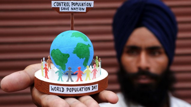 Artista indiano Gurpreet Singh posa com um globo e silhuetas representando a população mundial em Amritsa, Índia