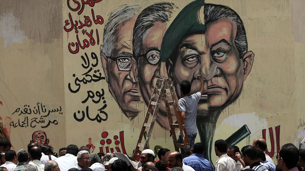 Na véspera das eleições presidenciais do Egito, artista escreve, em árabe, em muro da capital Cairo a frase "Nunca lhes daremos paz". Ao lado, um painel em grafite com caricaturas do presidente deposto Hosni Mubarak, do líder militar Hussein Tantawi e dos candidatos presidenciais Amr Mussa e Ahmed Shafiq