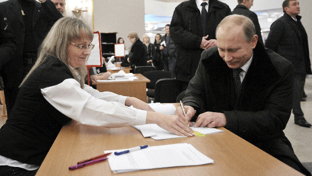O premiê Vladimir Putin assina seu nome numa mesa eleitoral
