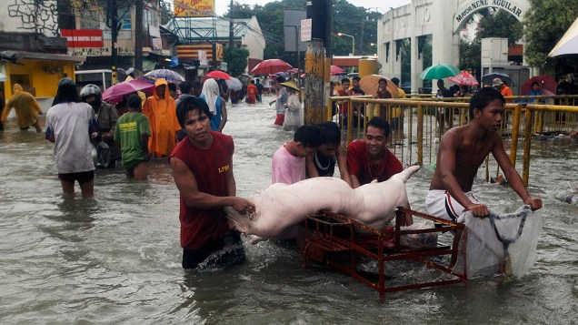 Homens carregam porco em via alagada na região metropolitana de Manila, nas Filipinas