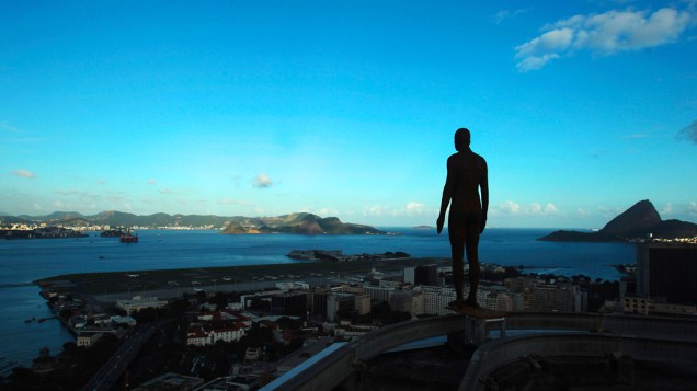 Figura de um homem feito de ferro e fibra de vidro pelo escultor britânico Antony Gormley, vista em telhado de um prédio no centro do Rio de Janeiro com vista para a Baía de Guanabara