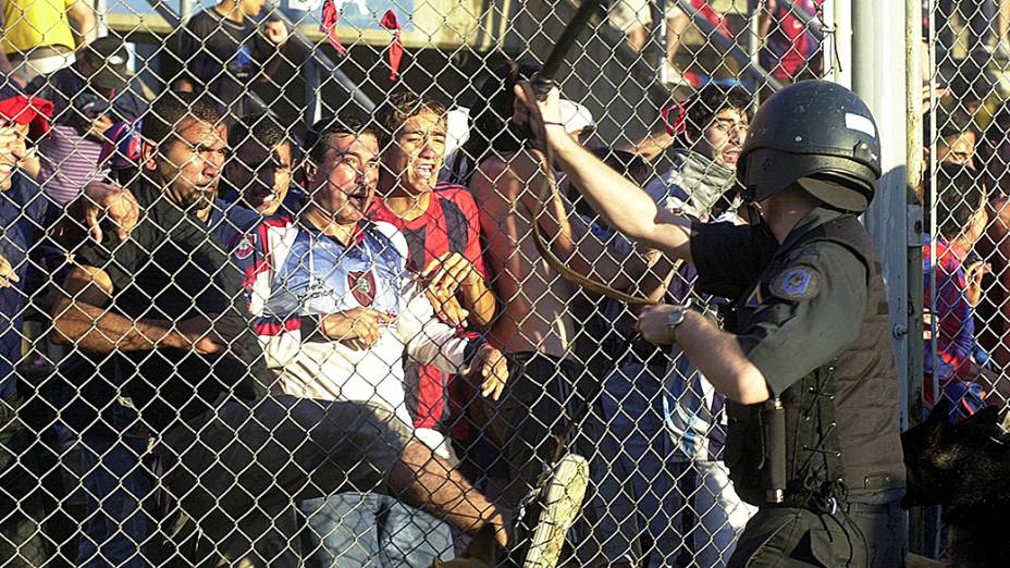 Torcedores do San Lorenzo tentam quebrar a grade que separa a arquibancada do campo ao serem reprimidos por um policial, em partida contra o Independiente