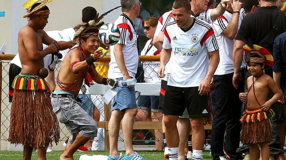 O jogador Lukas Podolski olha um índio brincando com a bola