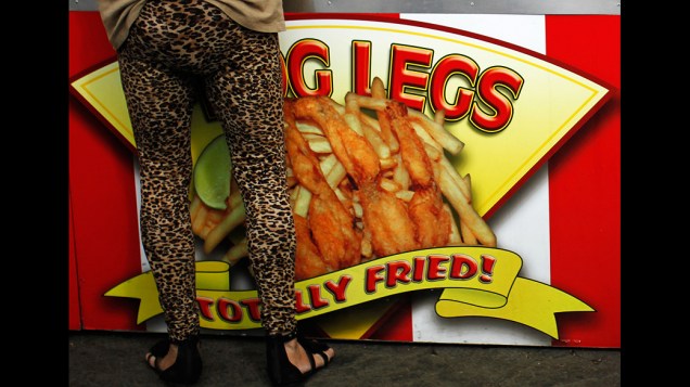 Mulher ao lado de um cartaz de rãs fritas durante a Los Angeles Country Fair, Califórnia