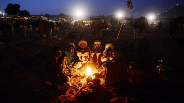 Grupo de negociantes se aquece próximo a fogueira ao amanhecer na feira de camelos em Pushkar, Índia