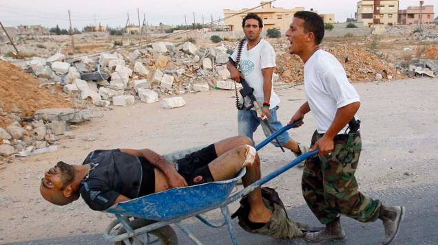 Rebeldes da Líbia transportam um franco-atirador ferido durante um ataque a um edifício em Trípoli  