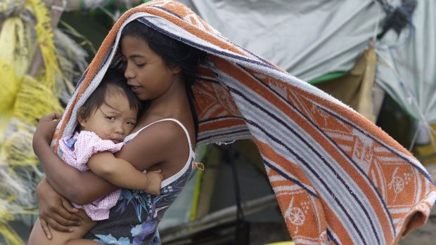 Garota protege bebê do vento em campo de desabrigados temporário em Navotas