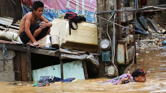 Jovem sobe no telhado de sua casa para fugir de inundação. Chuvas torrenciais e inundações têm provocado um caos na região em torno da capital filipina
