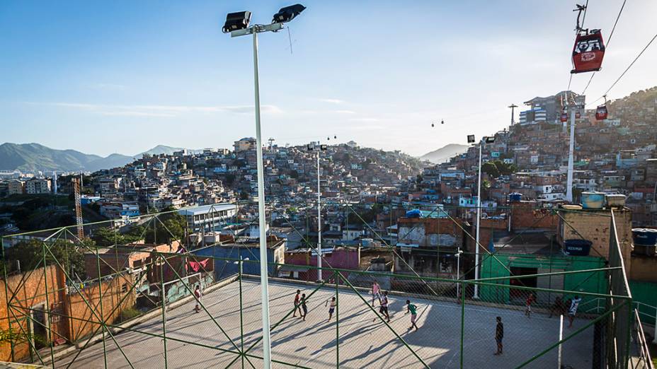 Partida de futebol disputada na quadra de uma comunidade enquanto o teleférico transporta moradores no Complexo do Alemão, no Rio de Janeiro