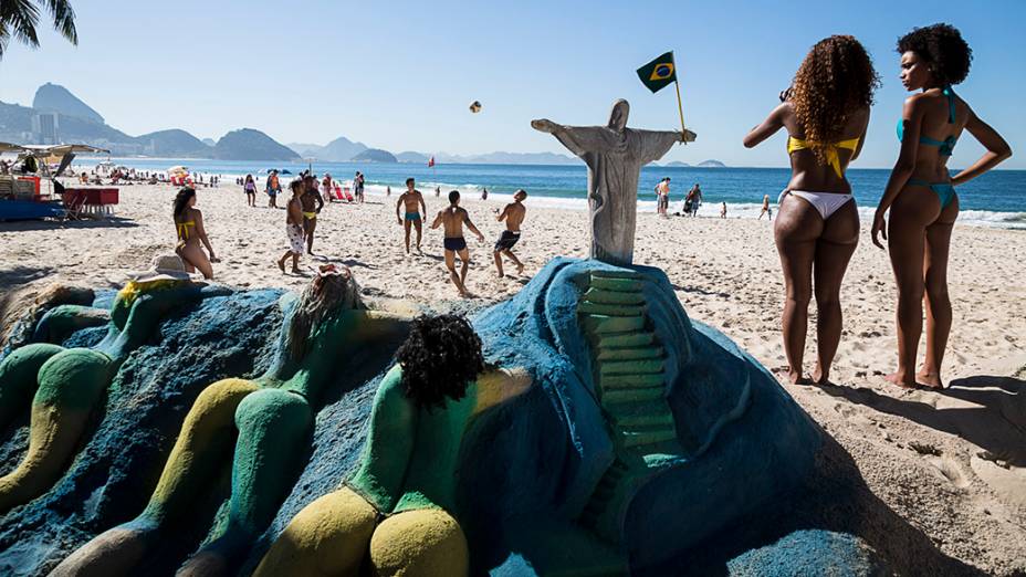 Um grupo de amigos joga futebol na praia de Copacabana próximo a uma escultura de areia representando cariocas tomando banho de sol, sob o olhar atento do Cristo Redentor - Rio de Janeiro, 2013