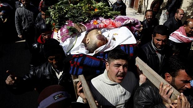 Homem carrega corpo durante funeral na Síria