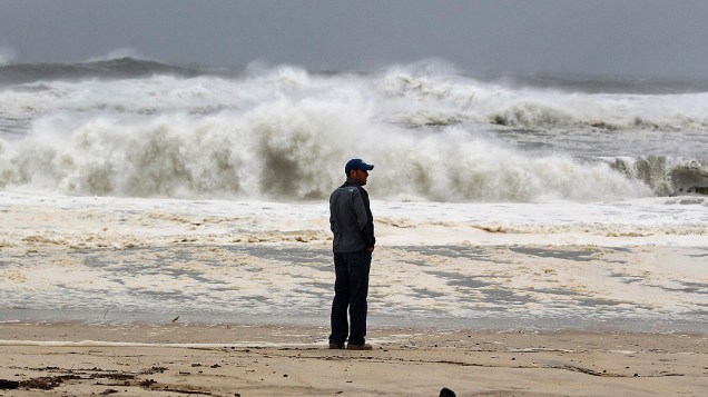 Homem olha para a costa enquanto as ondas provocadas pela passagem do Sandy se aproximam. Bolsa de Nova York fecha por causa de furacão Sandy