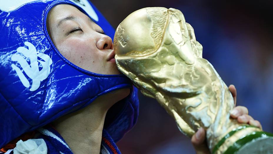 Torcedora beija réplica do troféu enquanto aguarda o início da partida entre Japão e Costa do Marfim, na Arena Pernambuco