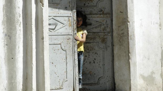 Menina síria espia a rua de sua casa em Hama