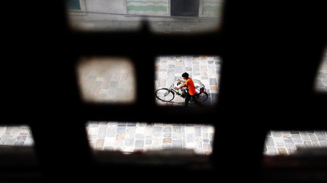 Menino é visto através da janela de uma casa empurrando sua bicicleta nas ruas de Kathmandu, no Nepal