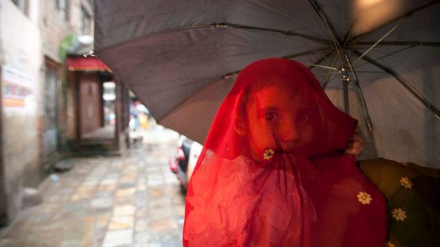 Garota é protegida da chuva pela mãe em Katmandu, Nepal