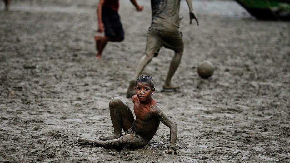 Meninos jogam futebol em um rio lamacento perto de uma aldeia em Yangon, Mianmar