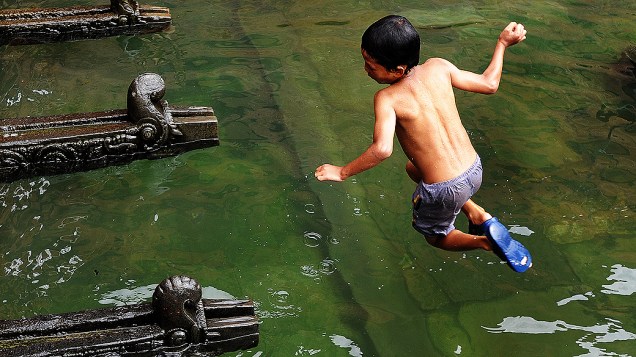 Garoto pula em piscina cuja água foi coletada de uma bica em Lalitpur, no Nepal