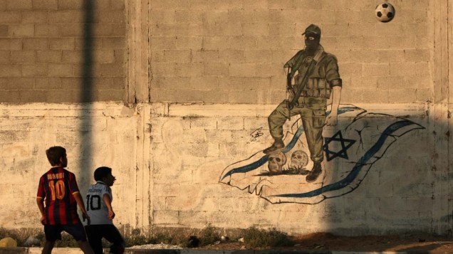 Garotos jogam futebol em frente a grafite anti-Israel na Cidade de Gaza