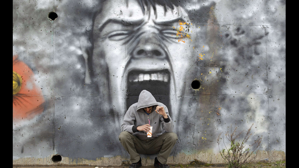Homem toma café em frente a um grafite na Grécia