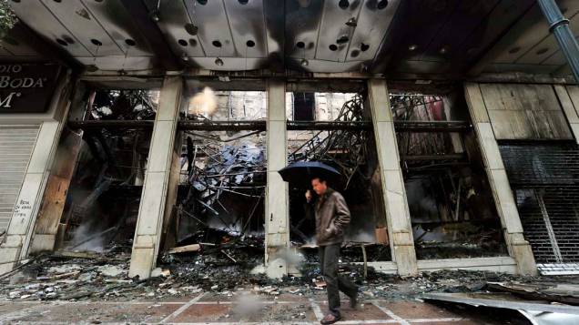 Homem passa em frente a loja incendiada em Atenas, após noite de violência devido à aprovação de um novo pacote de austeridade econômica