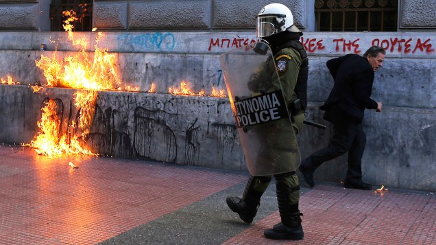 Policial passa próximo de fogo provocado por um coquetel molotov jogados por manifestantes em Atenas