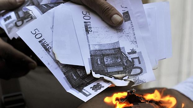 Manifestante queima cópias de cédulas do euro diante do Banco Central da Grécia, em protesto no último sábado