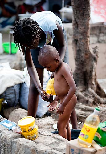 Menina dá banho em criança em acampamento na praia Boyer em Petion Ville.