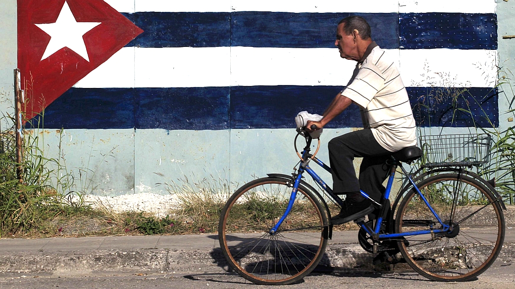 De bicicleta em uma rua de Havana, o homem passa em frente a um muro com uma bandeira de Cuba pintada