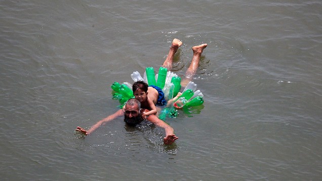 Homem usa garrafas plásticas para ajudar sua filha a nadar nos arredores de Lahore, no Paquistão