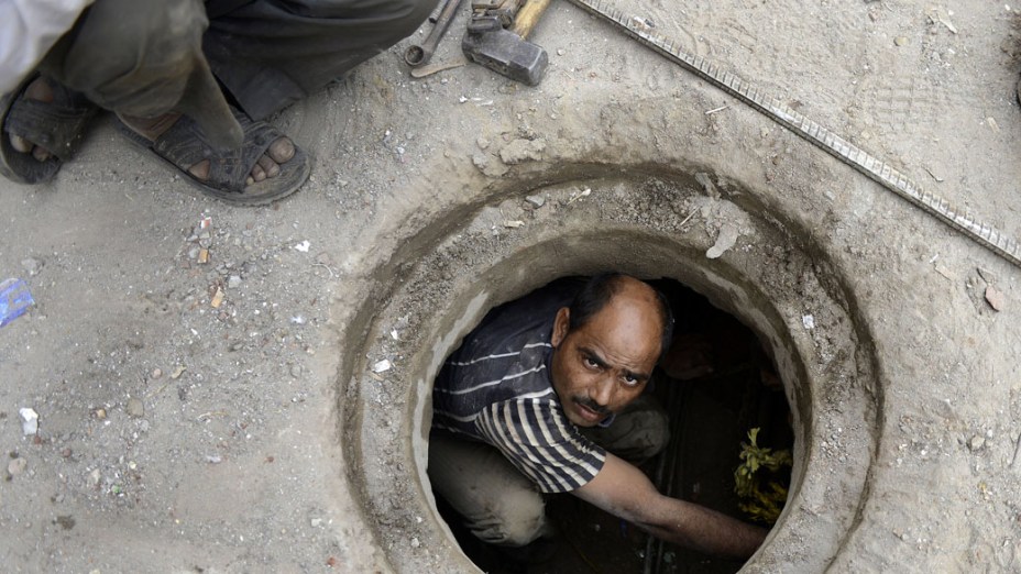 Encanador trabalha em tubulação subterrânea de Nova Délhi, na Índia