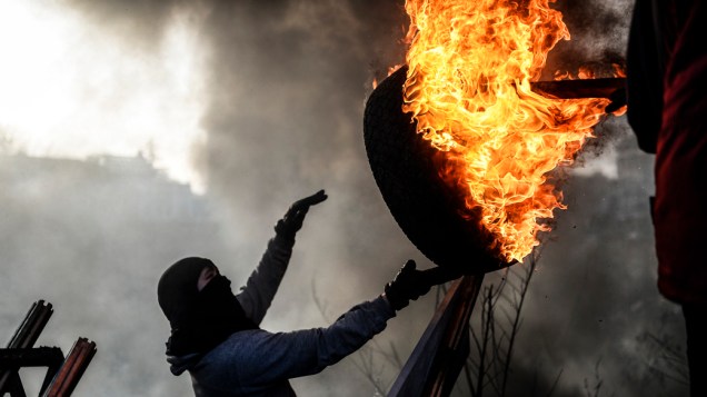 Manifestante arremessa pneu em chamas durante confrontos em Kiev, na Ucrânia