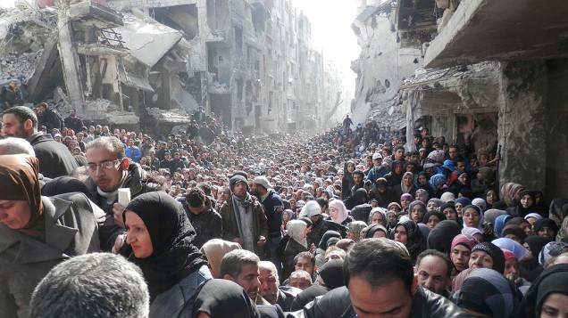 Em imagem divulgada nesta quarta-feira (26), multidão de moradores do bairro al-Yarmouk, transformado em campo de refugiados no sul de Damasco, aguarda a distribuição de alimentos pela agência UNRWA, da ONU