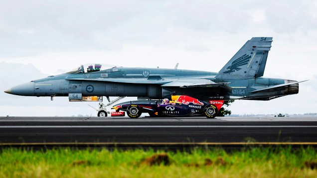 Daniel Ricciardo, piloto de Fórmula 1, dirige seu carro Infiniti Red Bull ao lado de um avião da Força Aérea australiana, durante um evento promocional na base aérea de Melbourne