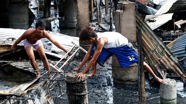 Moradores ficam sobre as ruínas de suas casas, destruídas por um incêndio em Malabon, região metropolitana de Manila (Filipinas), nesta quarta-feira (12)