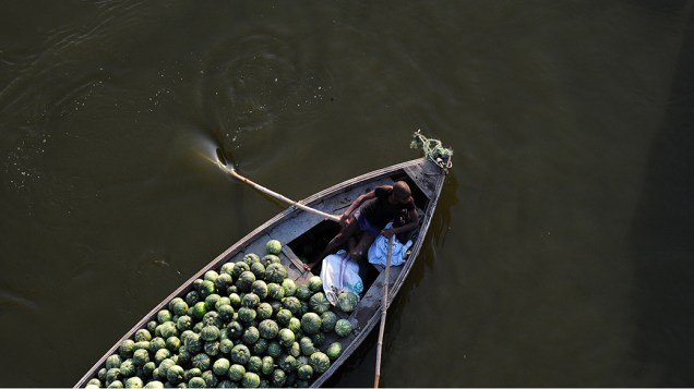 Trabalhador transporta abóboras em um barco na cidade de Allahabad, Índia Trabalhador transporta abóboras em um barco na cidade de Allahabad, Índia