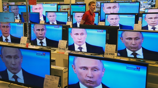 Funcionário de uma loja em Moscou caminha entre televisores durante a transmissão de um pronunciamento do presidente Vladimir Putin sobre a crise da Ucrânia