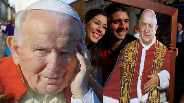 Em Roma, fiéis posam com fotos dos Papas João Paulo II e João XXIII que serão canonizados em cerimônia no próximo domingo