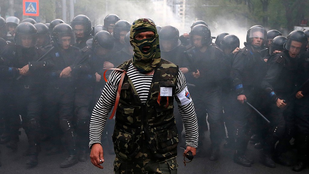 Manifestante pró-Rússia caminha na frente da polícia de choque durante uma manifestação pró-Ucrânia na cidade de Donetsk